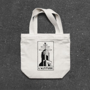 Tote bag with the Altitude logo place on a rough concrete floor. Audiophile bar merchandise for music lovers, ideal for fans of vinyl mixes and high-quality sound experiences