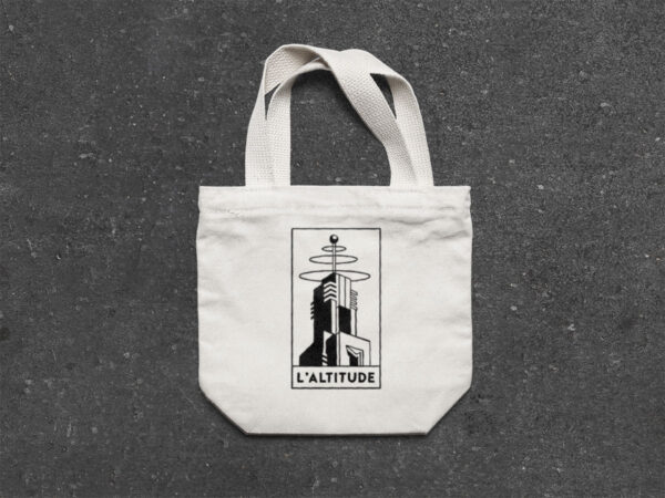 Tote bag with the Altitude logo place on a rough concrete floor. Audiophile bar merchandise for music lovers, ideal for fans of vinyl mixes and high-quality sound experiences